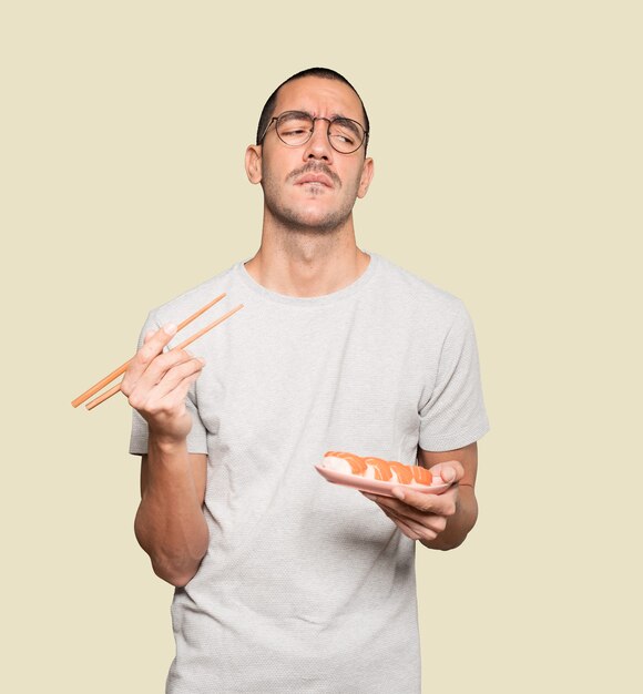 Young man using chopsticks to eat sushi