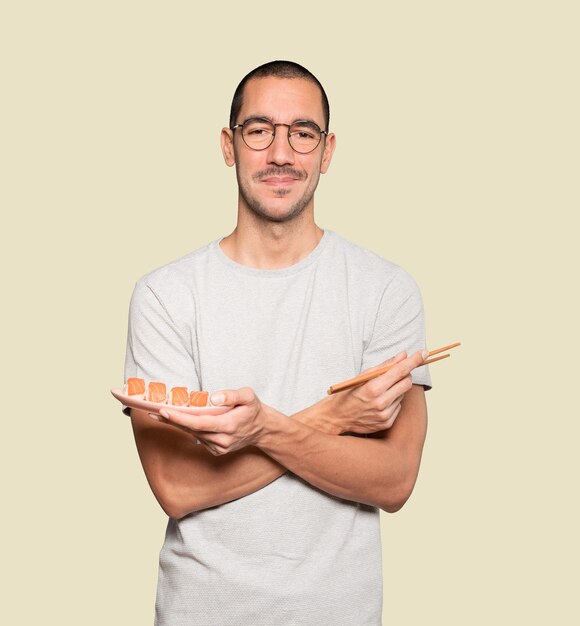 Молодой человек, используя палочки для еды, чтобы съесть суши