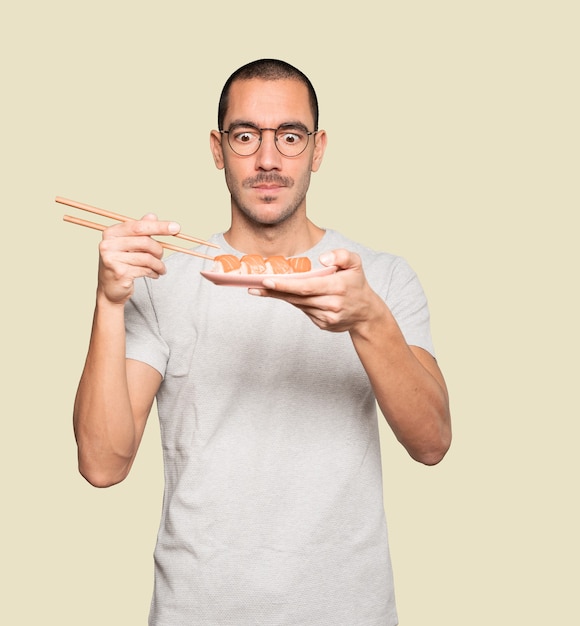 Young man using chopsticks to eat sushi