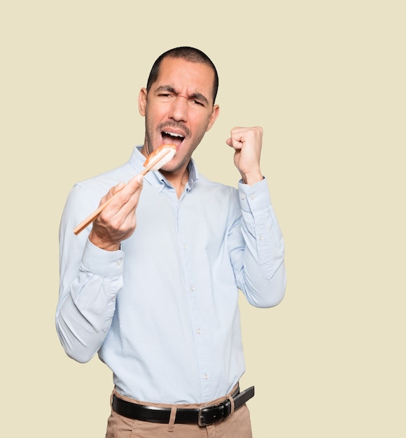 Young man using chopsticks to eat sushi