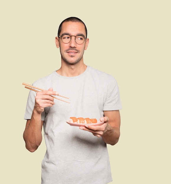 Young man using chopsticks to eat sushi