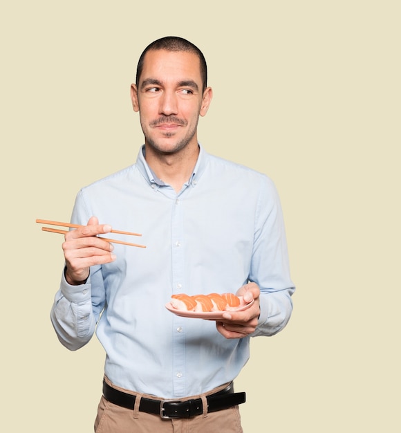 Young man using chopsticks to eat sushi