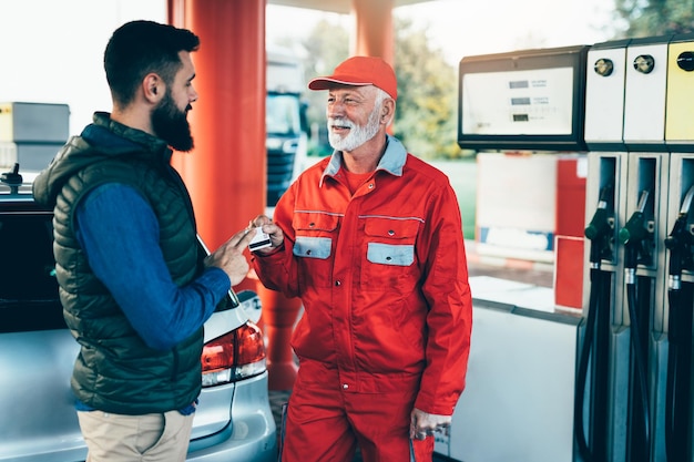 Young man using credit card to make a payment for refueling car on gas station.