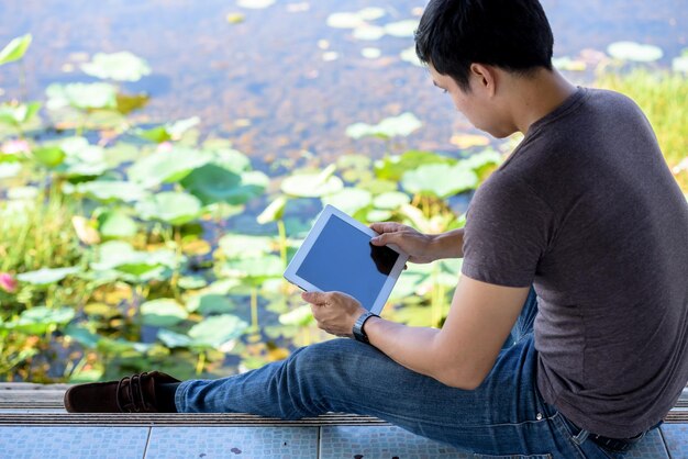 写真 デジタルタブレットを使う若い男が湖の近くの埠頭で