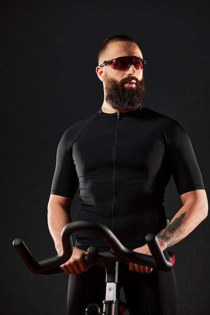 Молодой человек на велотренажере в спортзале мужчина с бородой и в очках на велотренажере фитнес