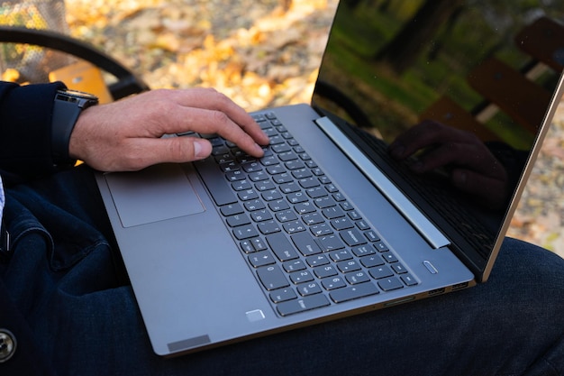 Young man using laptop in the autumn park closeup