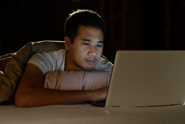 Young man using laptop computer in his bed at night