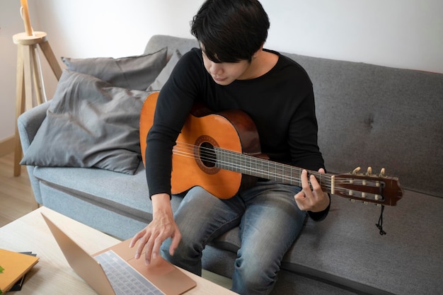 Young man using laptop computer and playing guitar on sofa