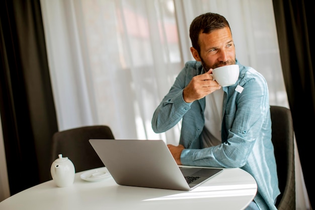 Молодой человек использует ноутбук и пьет чай в гостиной