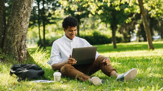 Photo young man using laptop sitting at park