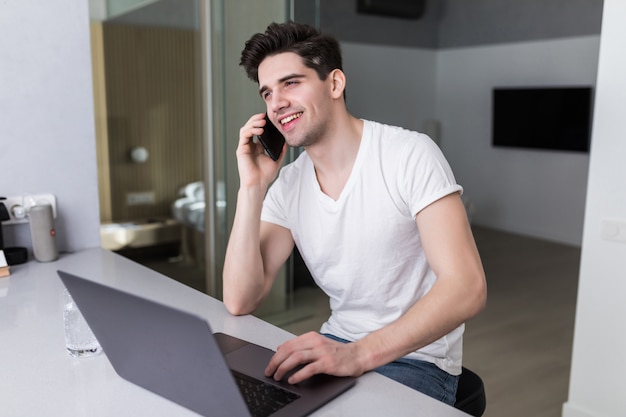 Young man using a laptop while on the phone at home