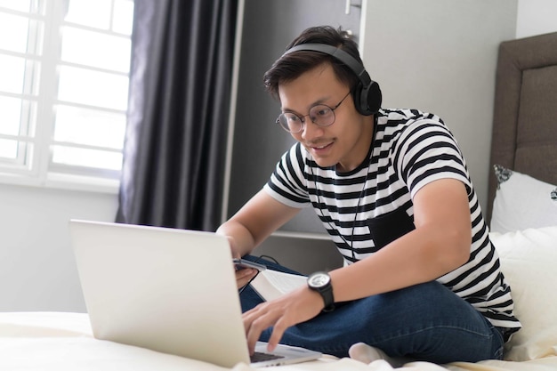 young man using laptop while sitting on bed at home