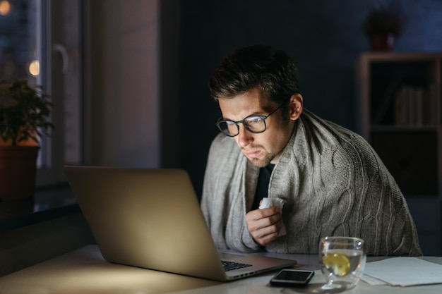 Foto giovane che utilizza il computer portatile mentre soffre di freddo