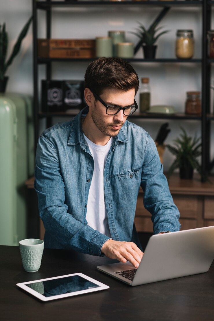 Photo young man using laptop with coffee cup and digital tablet on kitchen counter