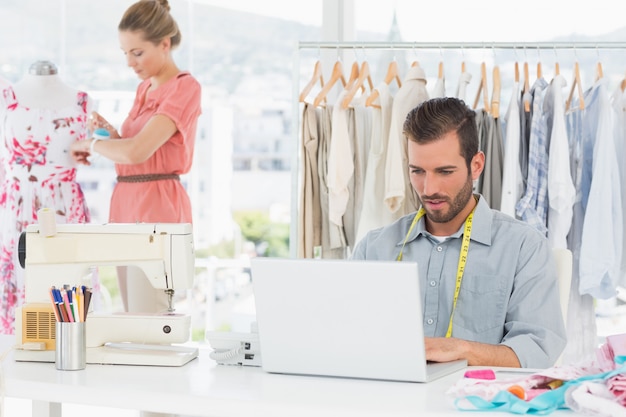 Young man using laptop with female fashion designer working in background at the studio