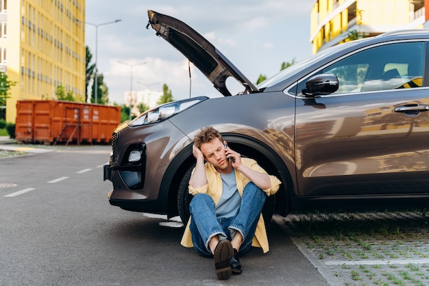 Young man using a mobile phone near a broken car in the city