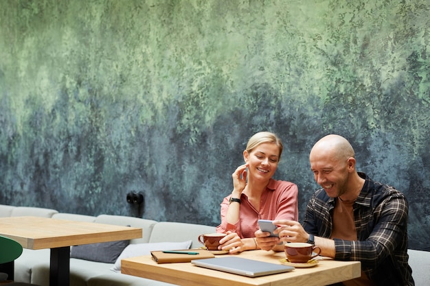 Young man using mobile phone while drinking coffee in cafe together with his girlfriend