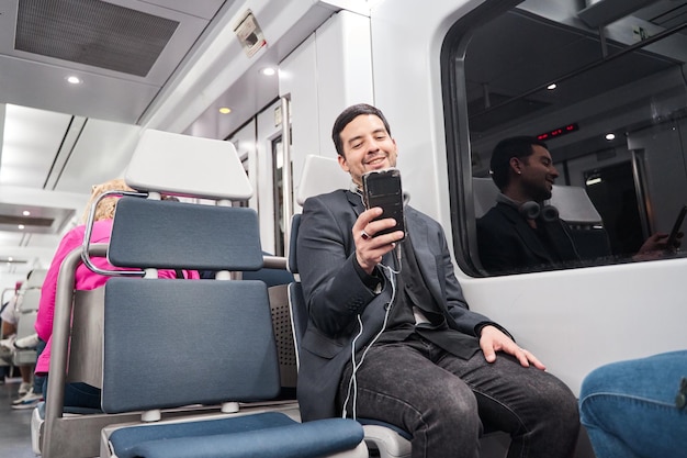 Young man using mobile phone while sitting on the subway train and listening to music