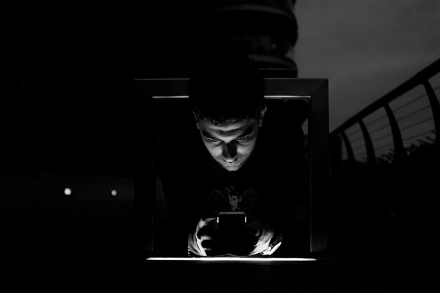 Young man using phone by railing at night