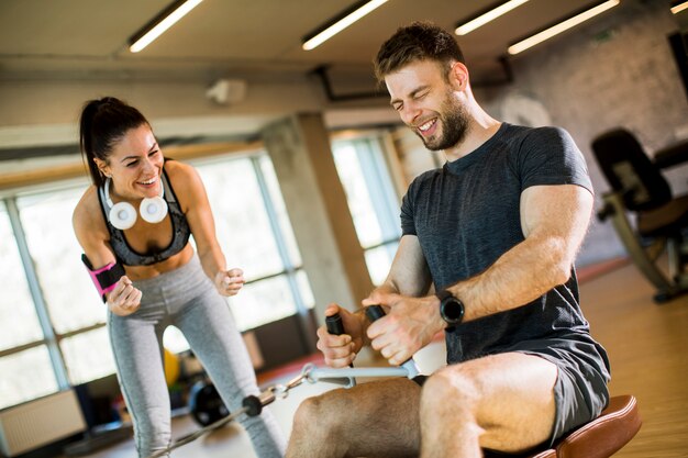 Young man using seated row machine in the gym with support of female coach