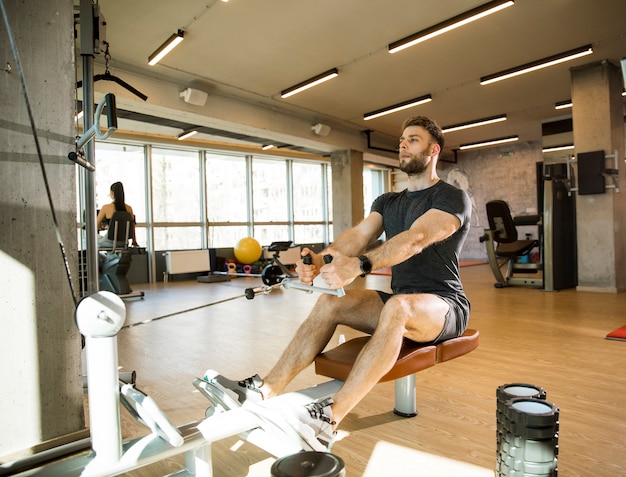 Young man using seated row machine in the gym