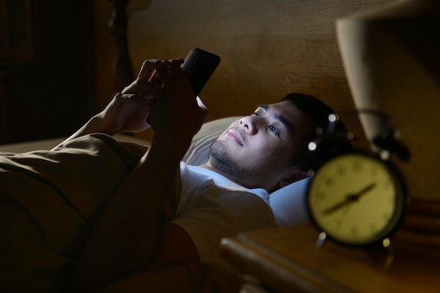 Photo young man using a smartphone in his bed at night