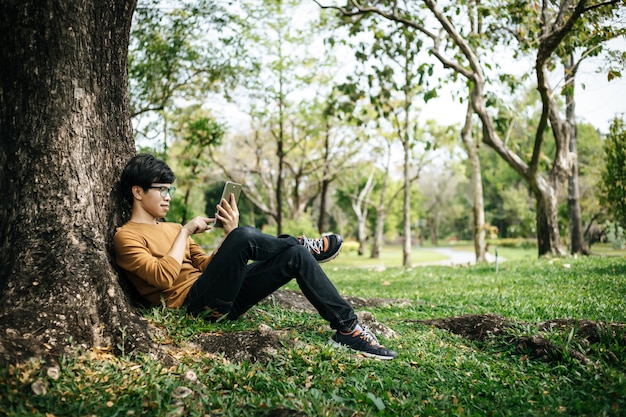 young man using a tablet and sitting under the tree