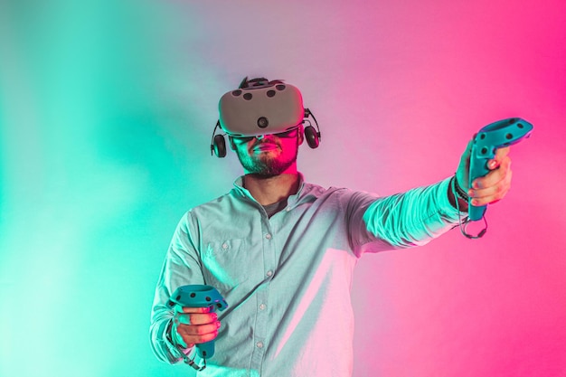 Молодой человек, использующий очки виртуальной реальности, два геймпада и играющий в видеоигры