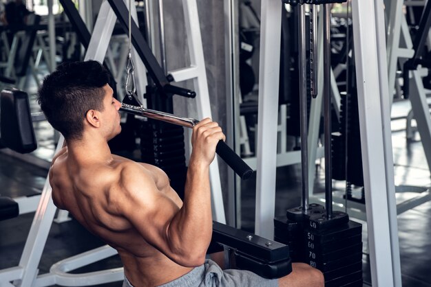 Young man using weight lifting equipment to build a massive chest and arm at indoor sport gym.