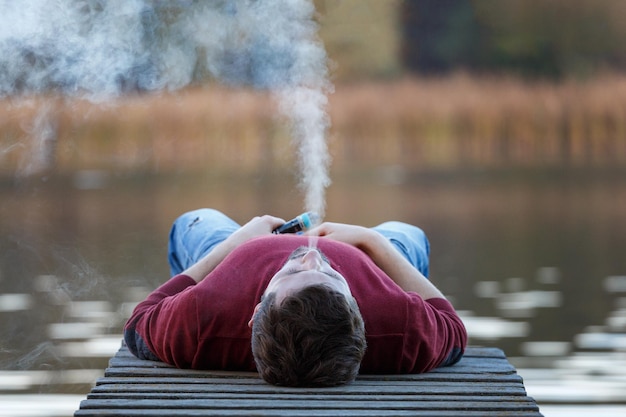 A young man  a vaper lies on a bridge on an autumn day and smokes