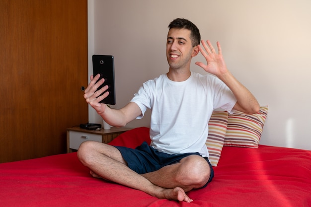 Young man on video call with his tablet from bed