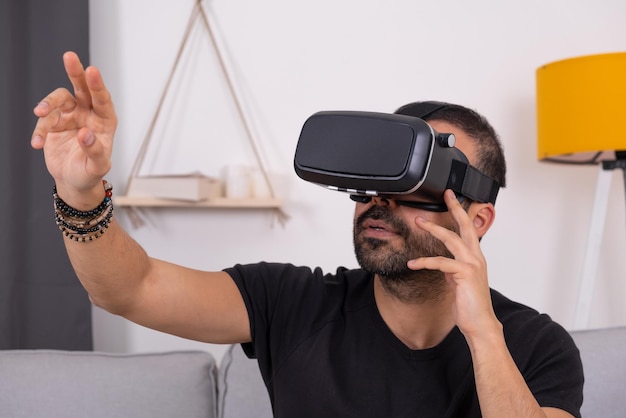 VRメガネのヘッドセットをかぶった若い男性が自宅で仮想現実と対話しビデオゲームをジェスチャーしています