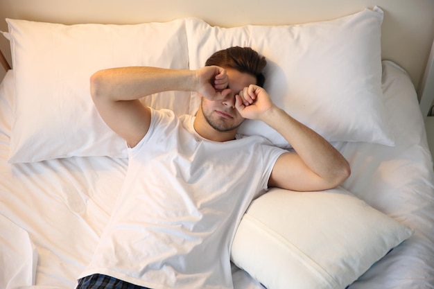 Young man waking up in bed at home