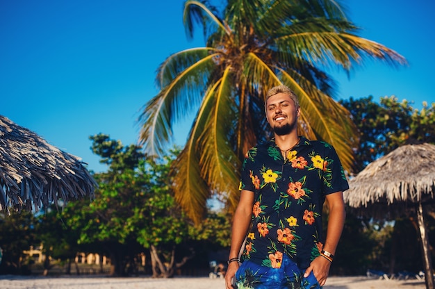 Foto giovane che cammina sulla spiaggia mentre sorride sullo sfondo delle palme