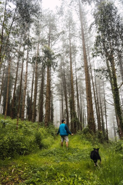 A young man walking in the blue jacket with the dog in the foggy forest