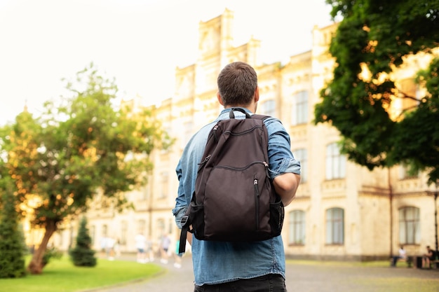 Young man walking down street with a backpack. Back view.