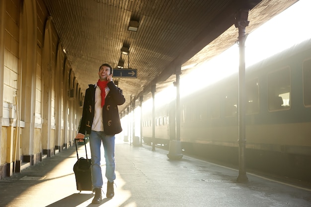 Young man walking at train station with bag and mobile phone