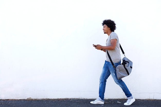 Foto giovane che cammina con la borsa e il telefono cellulare