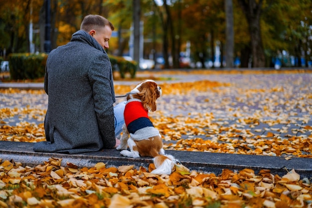 秋の公園で犬と一緒に歩いている若い男