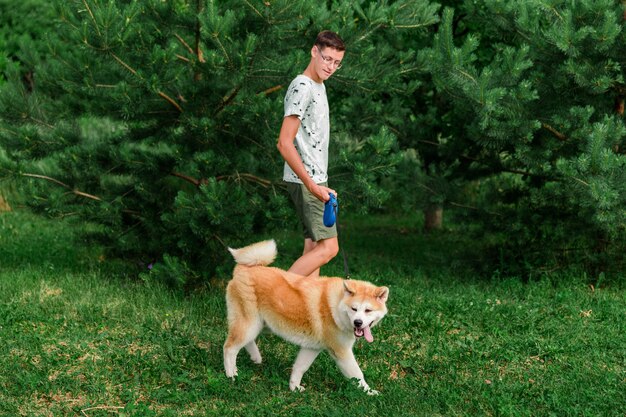 a young man walks in a summer park with a young puppy of akita breed