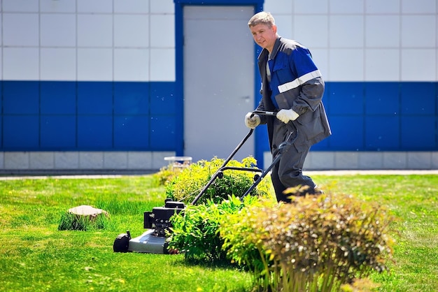 A young man walks with a lawn mower on a green lawn in a production area