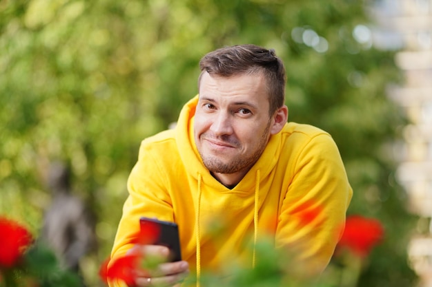 若い男が携帯電話を手にベンチに横になってカメラに向かって微笑んでいたスマートフォンを使用している男が住宅の中庭でインターネットを使用している