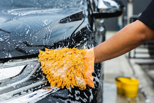 The young man washed his car with foamy cleansing foam. he was\
wearing gloves for washing the car. he wiped the headlights of the\
car.