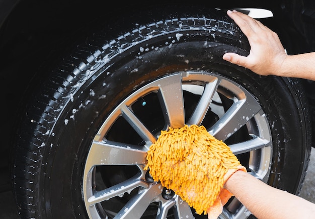 The young man washed his car with foamy cleansing foam. he was\
wearing gloves for washing the car. he wiped the wheels of the\
car.