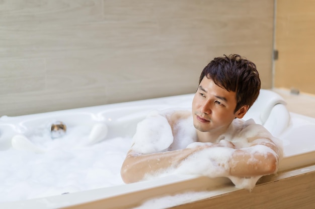 Young man washing body with foam in bathtub