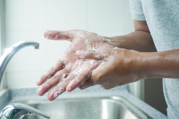 Giovane uomo lavarsi le mani con acqua calda e sapone