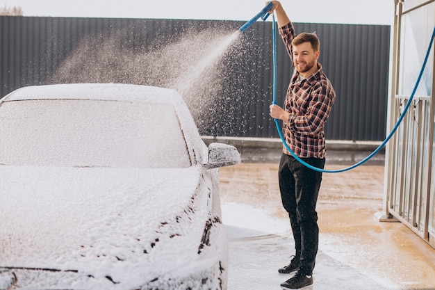 Carwash에서 그의 차를 세척하는 젊은 남자