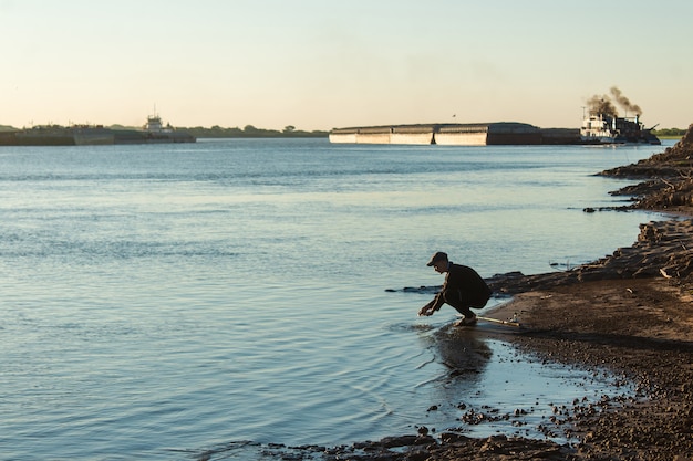 Young man washing his hands on the river bank.