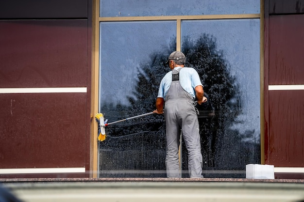 Young man washing window outdoors Professional cleaning Big panoramic windows