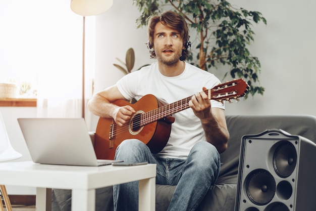 Young man watching guitar tutorial on his laptop at home